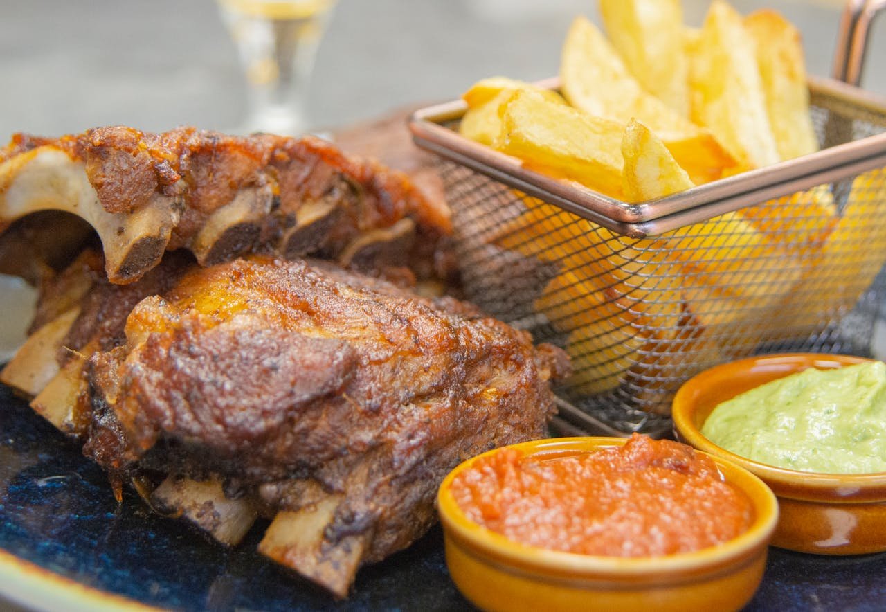 A close-up shot of grilled meat ribs, crispy fries, and dipping sauces, perfect for BBQ enthusiasts.